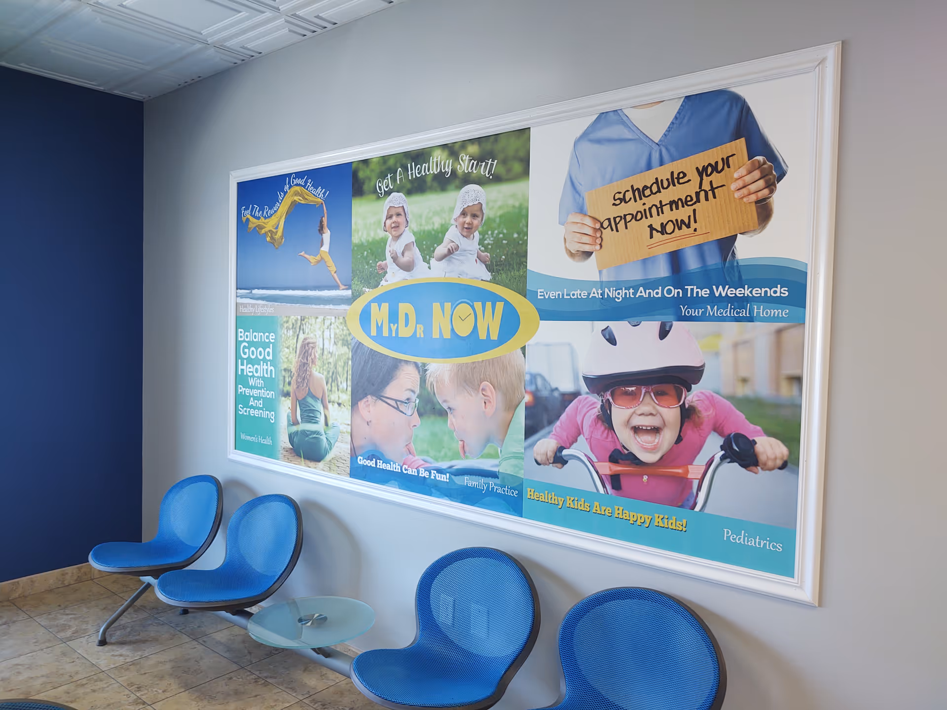 Interior waiting area with blue chairs and a large medical poster on the wall.