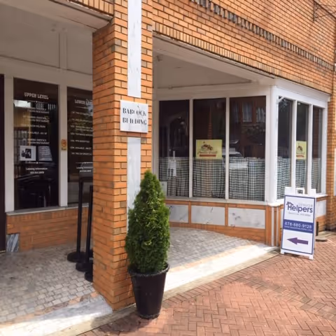 Brick facade entrance with glass storefront, potted shrub, and a Senior Helpers sign on display.