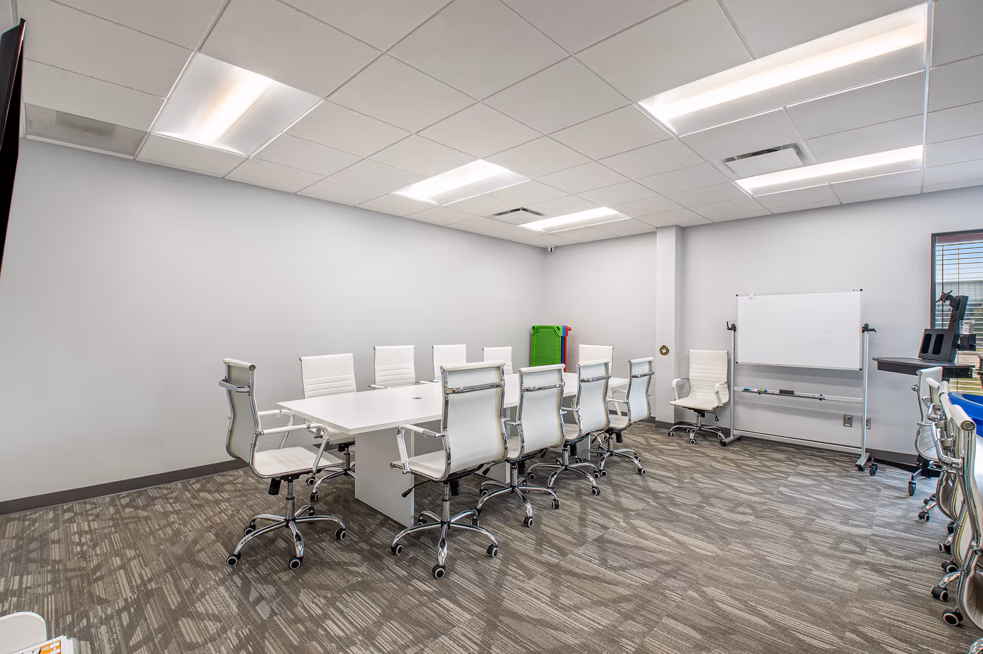 A bright conference room with a long white table and white chairs.