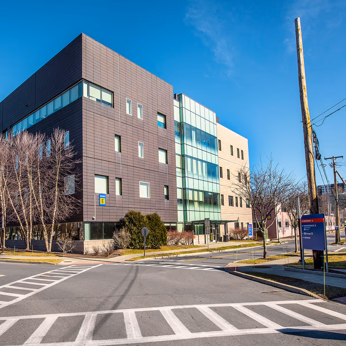 Modern multi-story medical building with glass entrance, adjacent street, crosswalk, and signage.