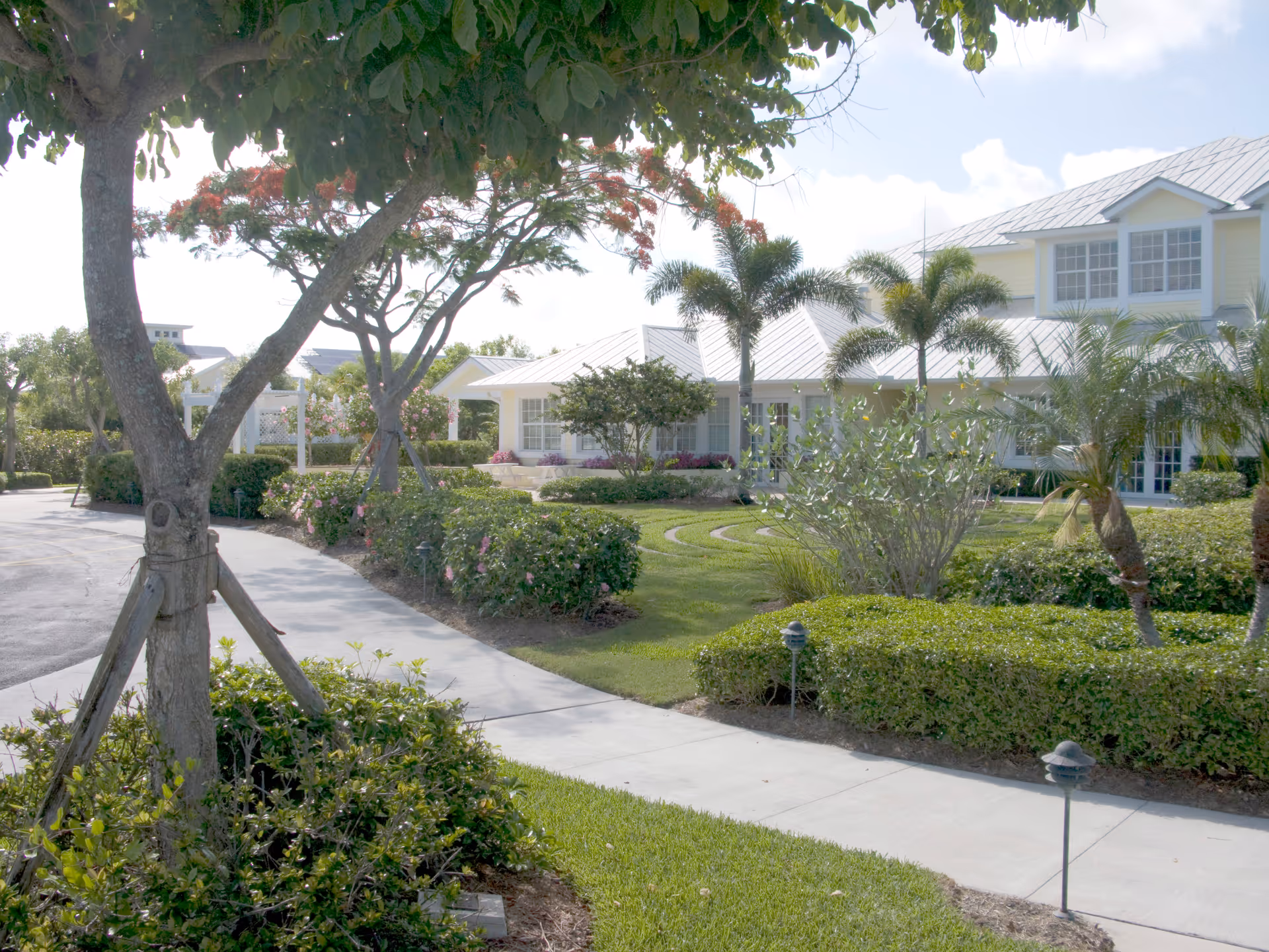 Sunlit walkway curves through manicured landscaping toward a light Treasure Coast Hospice building.