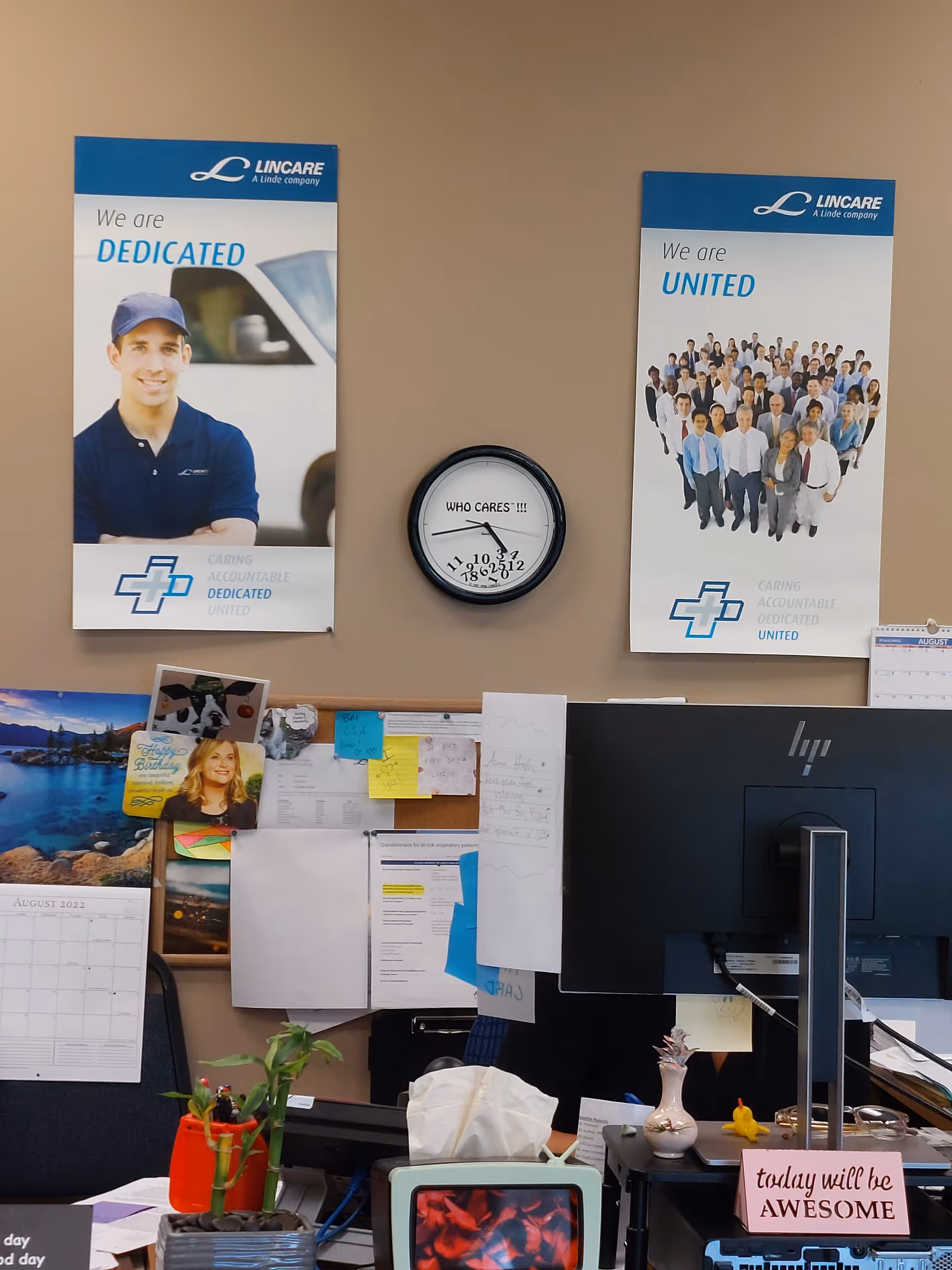 Indoor office area with Lincare posters, a clock, corkboard, and a computer monitor on beige wall.