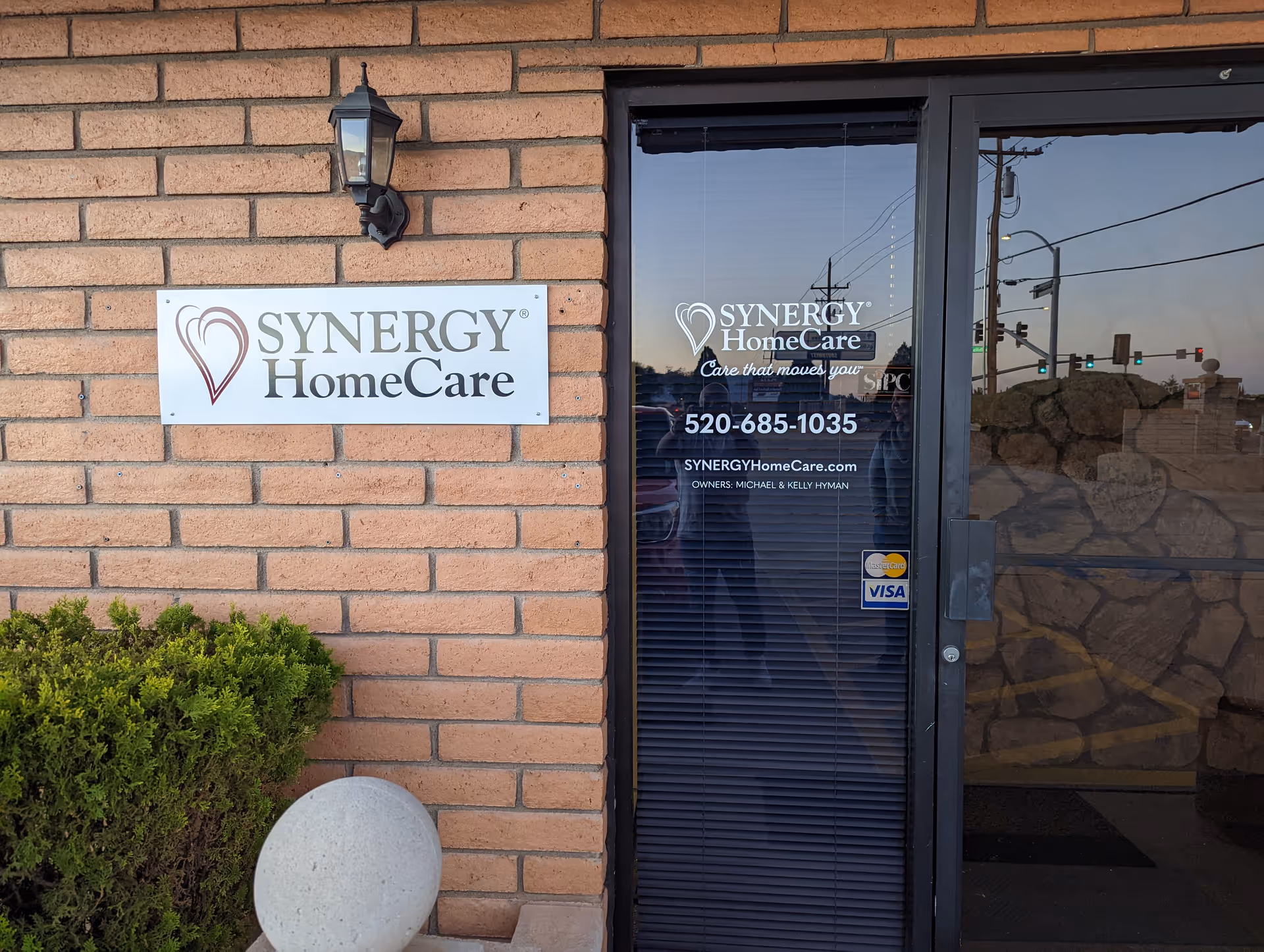 Brick exterior of Synergy HomeCare building with sign and glass entry door.