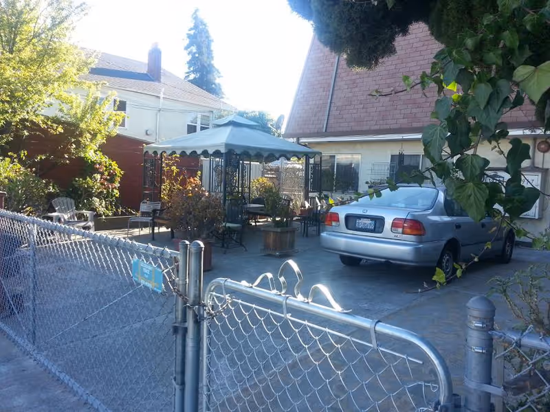 Outdoor patio with a car, canopy, chairs, potted plants, and a chain-link fence.