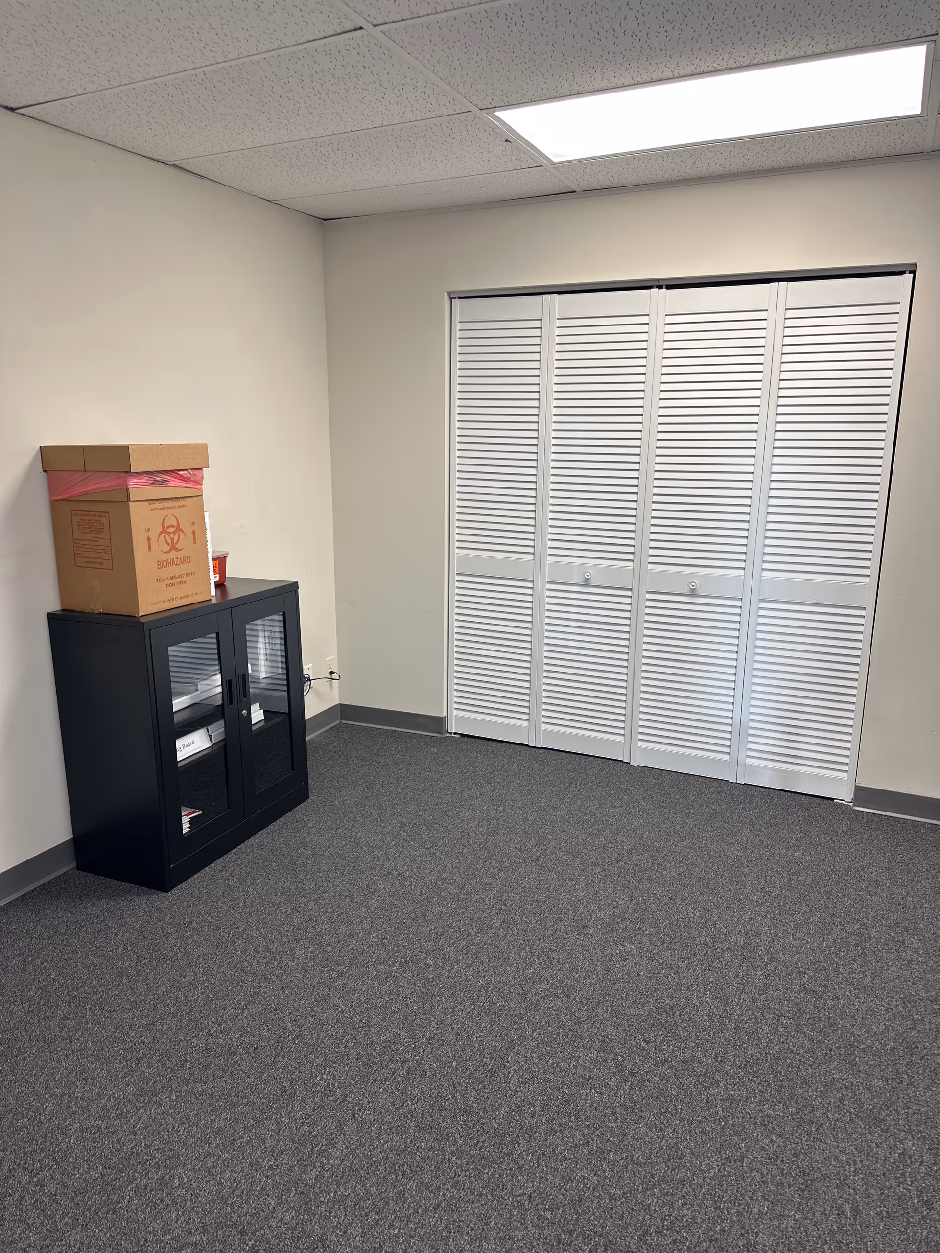 Empty interior room with a black cabinet, cardboard box, and white louvered closet doors.