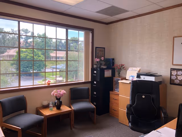 Interior office area in a senior living facility with large window, chairs, and filing cabinet.