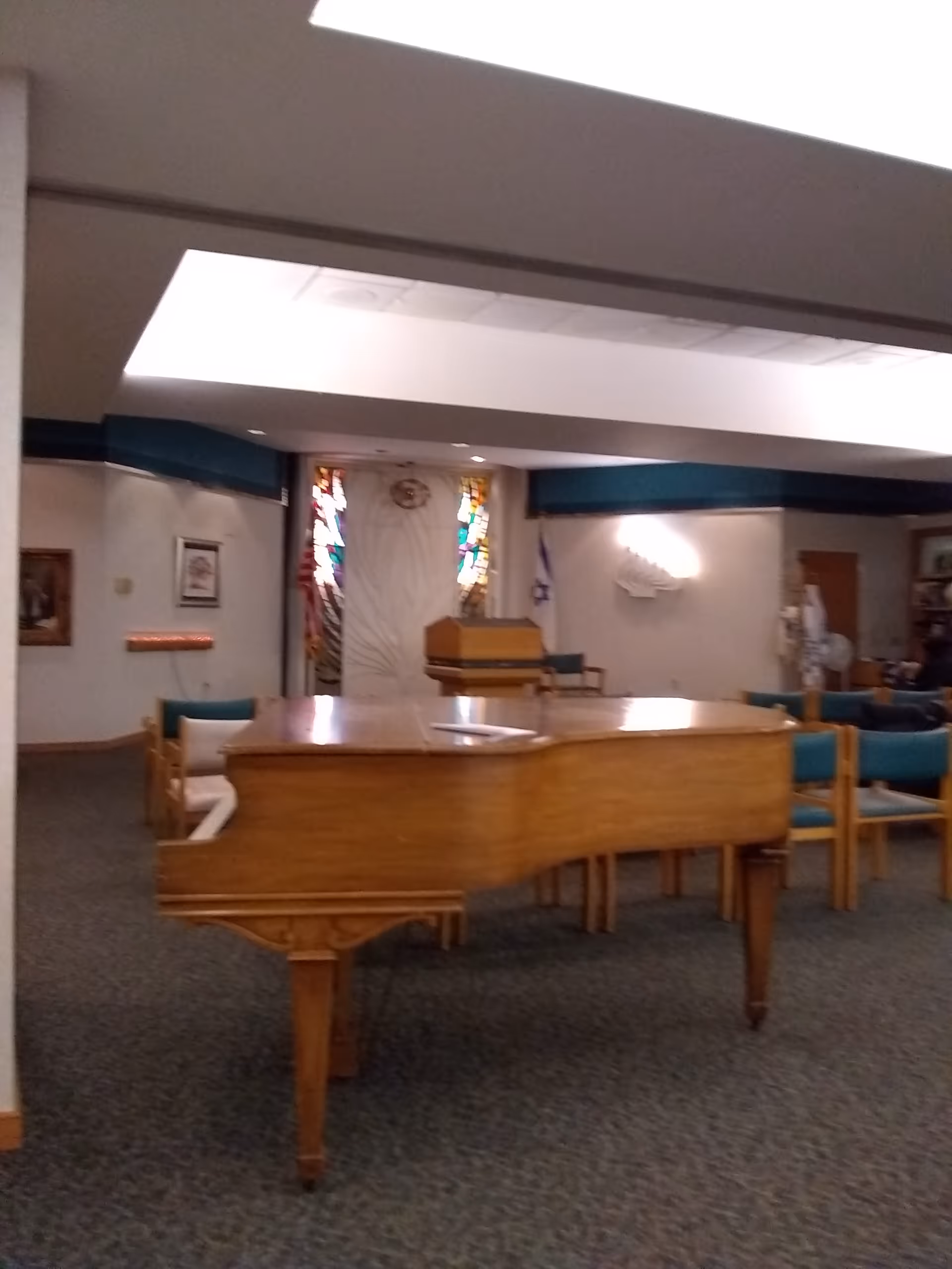 Wooden grand piano in a chapel-style lounge with stained glass and seating.