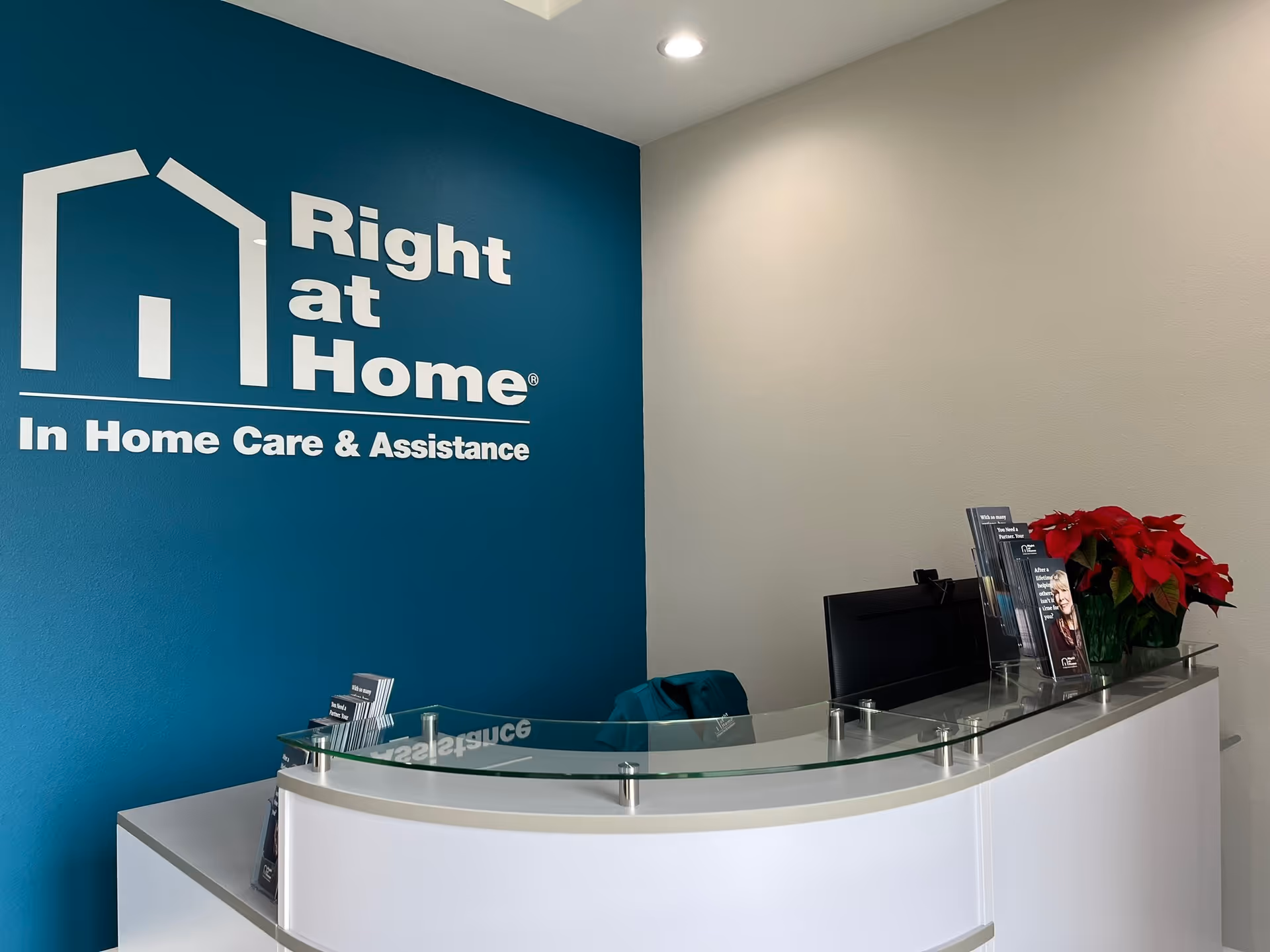 Reception area with a curved glass desk and teal wall featuring Right at Home logo.