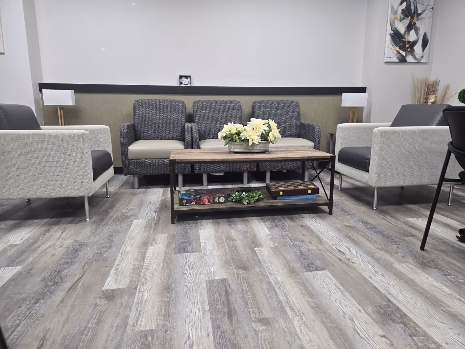 Modern senior living lounge with gray seating, a coffee table, and floral centerpiece.