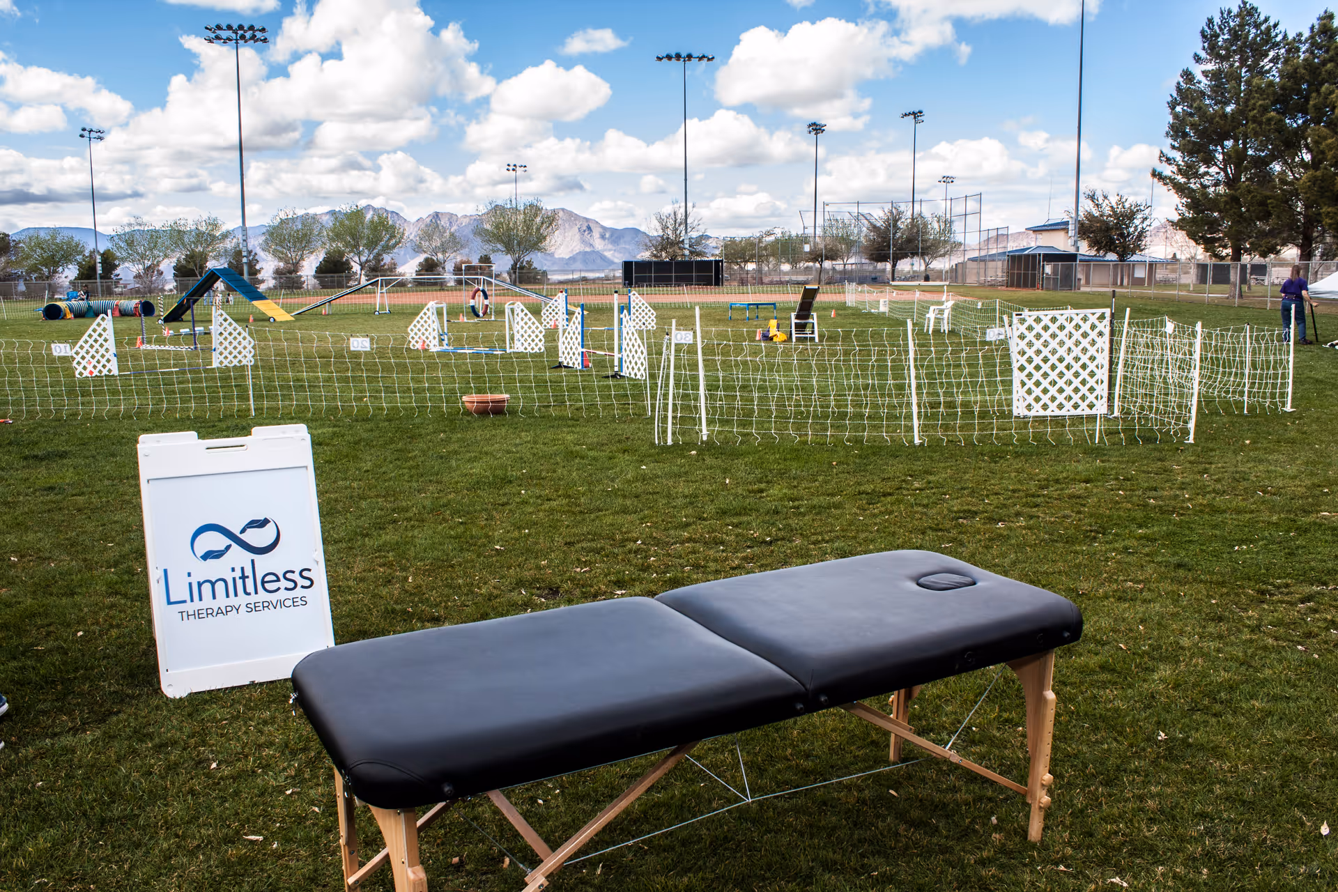 Outdoor field with agility equipment, fencing, and a massage table beside a Limitless Therapy Services sign.