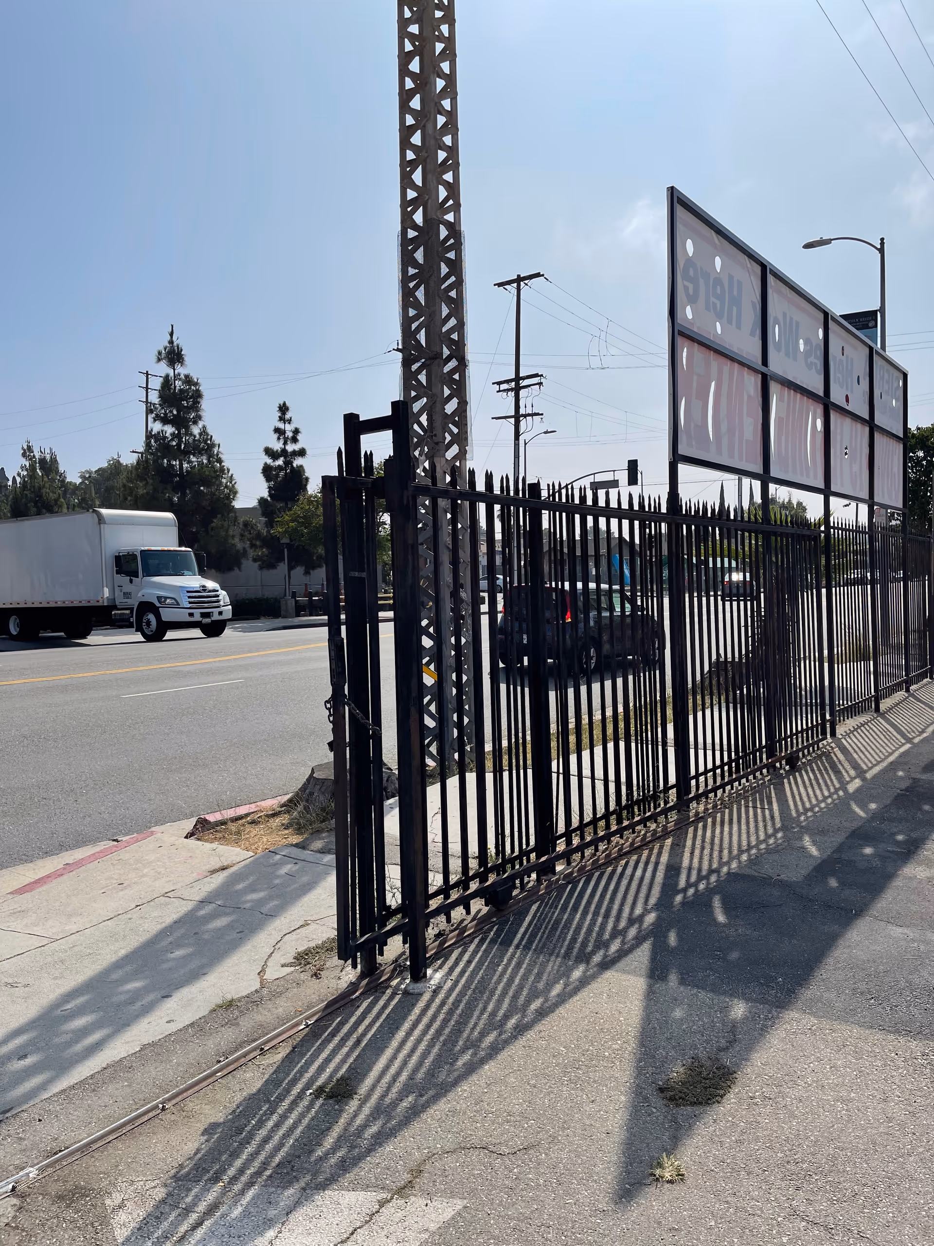 Tall black metal fence along a sidewalk with a street and sign.