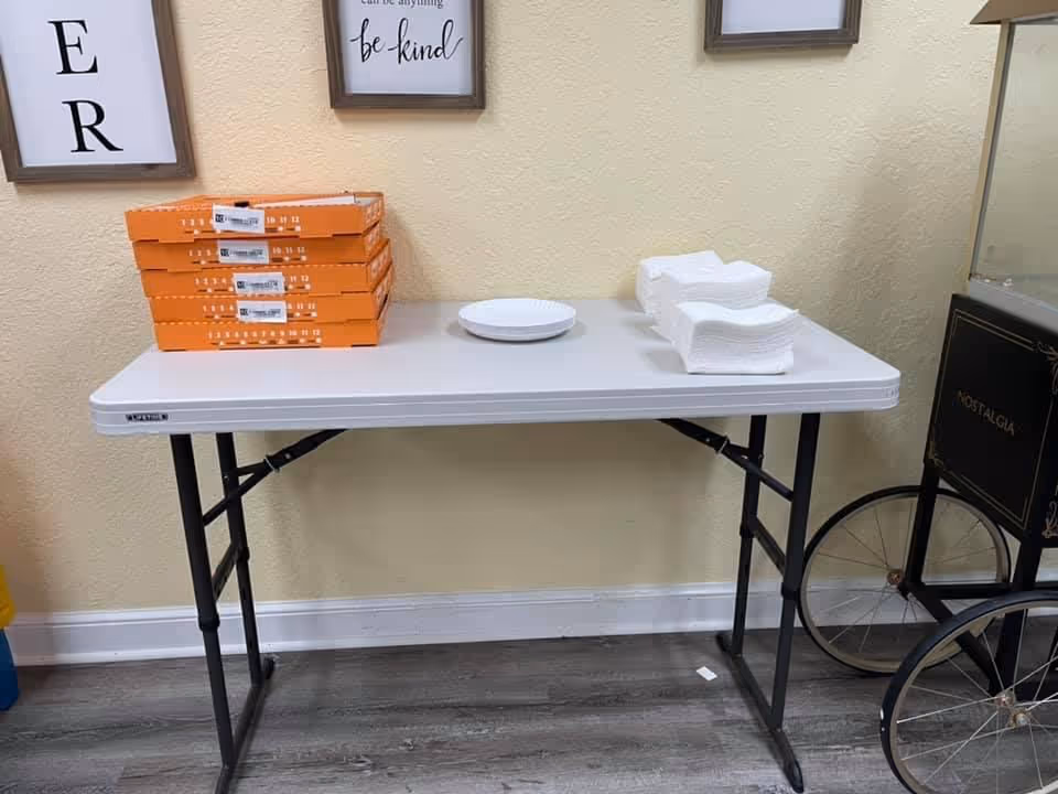 Folding table with stacked orange boxes, plates, and napkins against a wall.