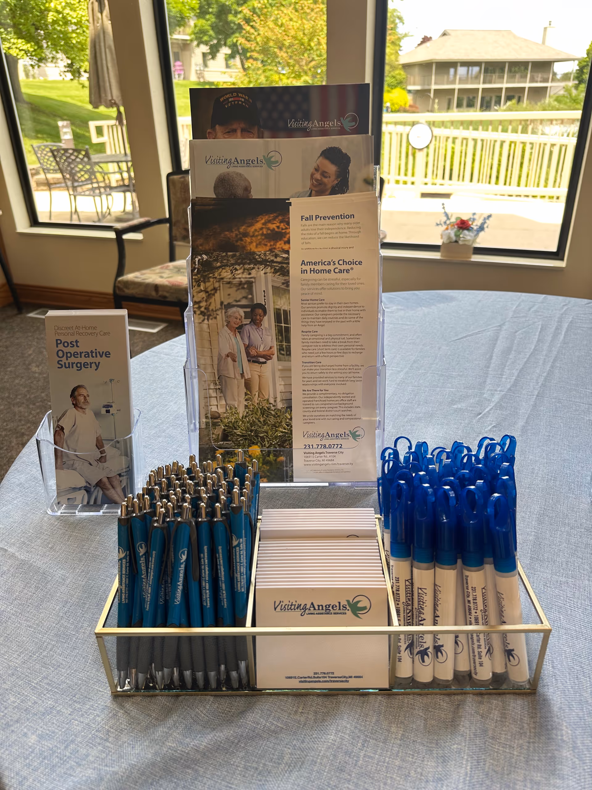 Promotional display with brochures, pens, and informational materials for Visiting Angels in a sunlit indoor room.