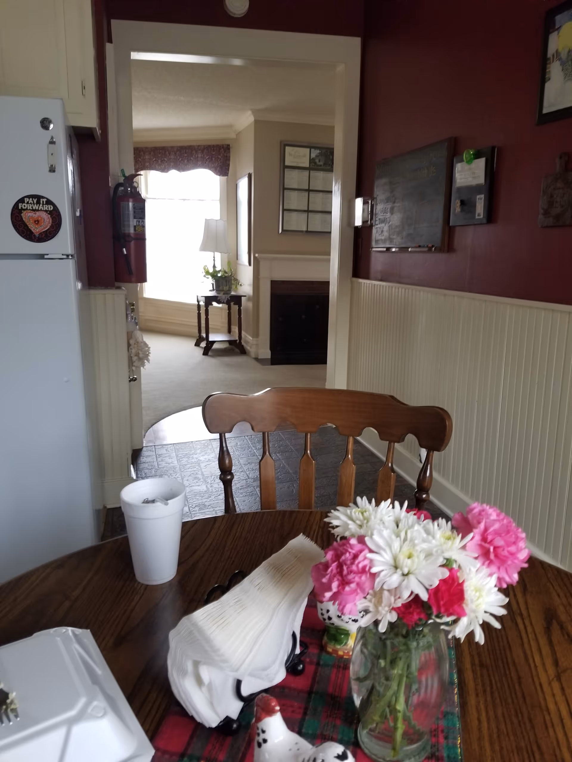 Wood dining table with pink flowers and napkins, leading to a cozy living area.