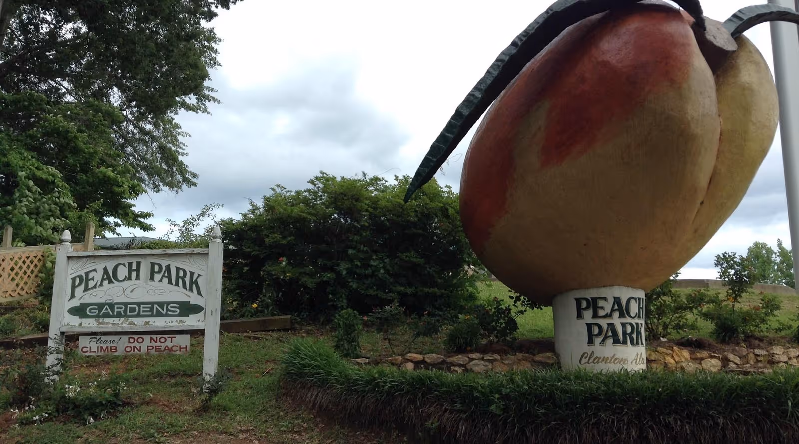 Outdoor scene featuring Peach Park Gardens sign and a giant peach sculpture.