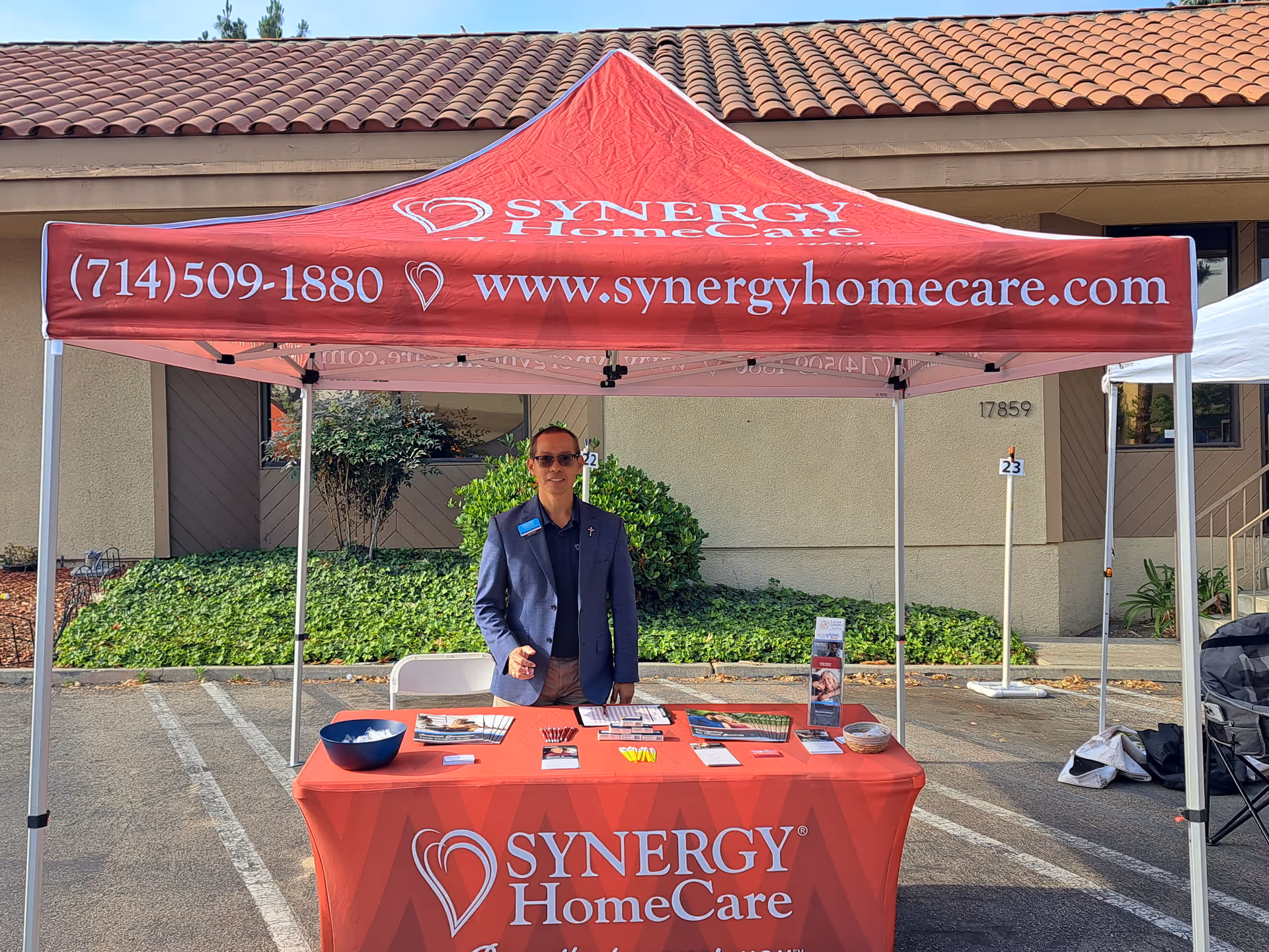 A Synergy HomeCare promotional tent with a staff member at a table in a parking lot.