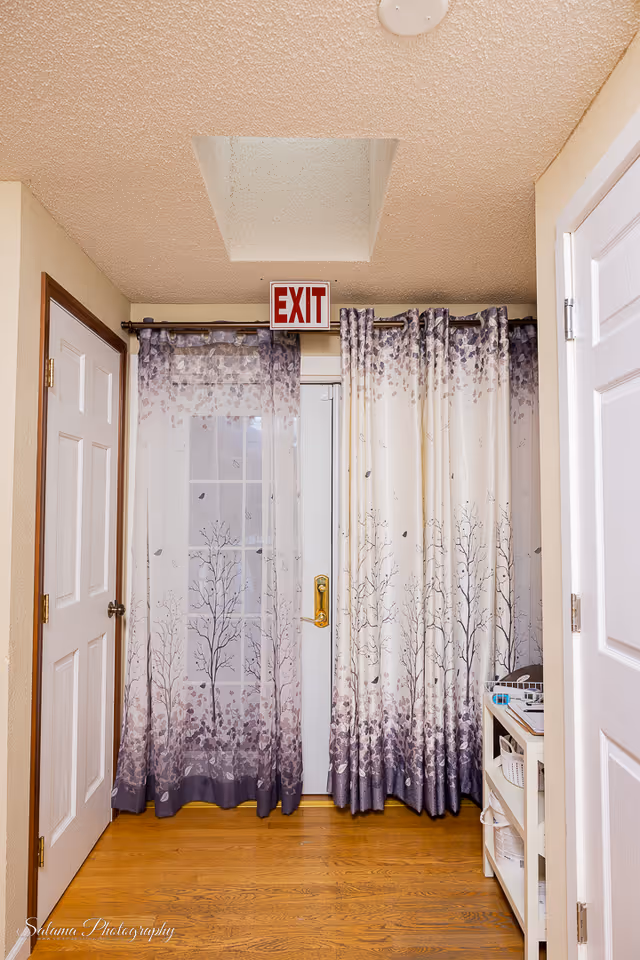 Interior hallway with double doors, patterned curtains, and an illuminated EXIT sign.