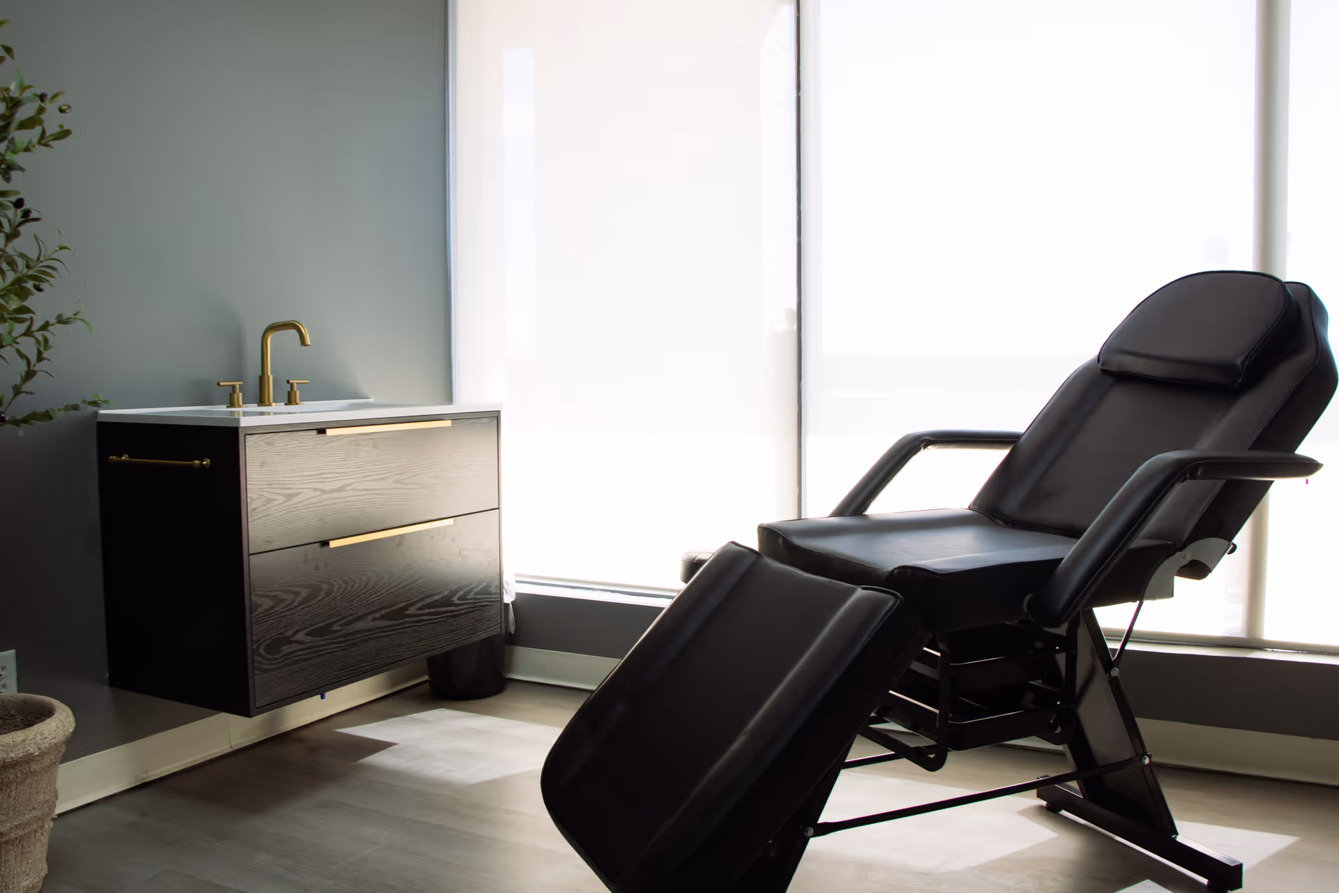 A reclining treatment chair beside a dark vanity with a gold faucet.