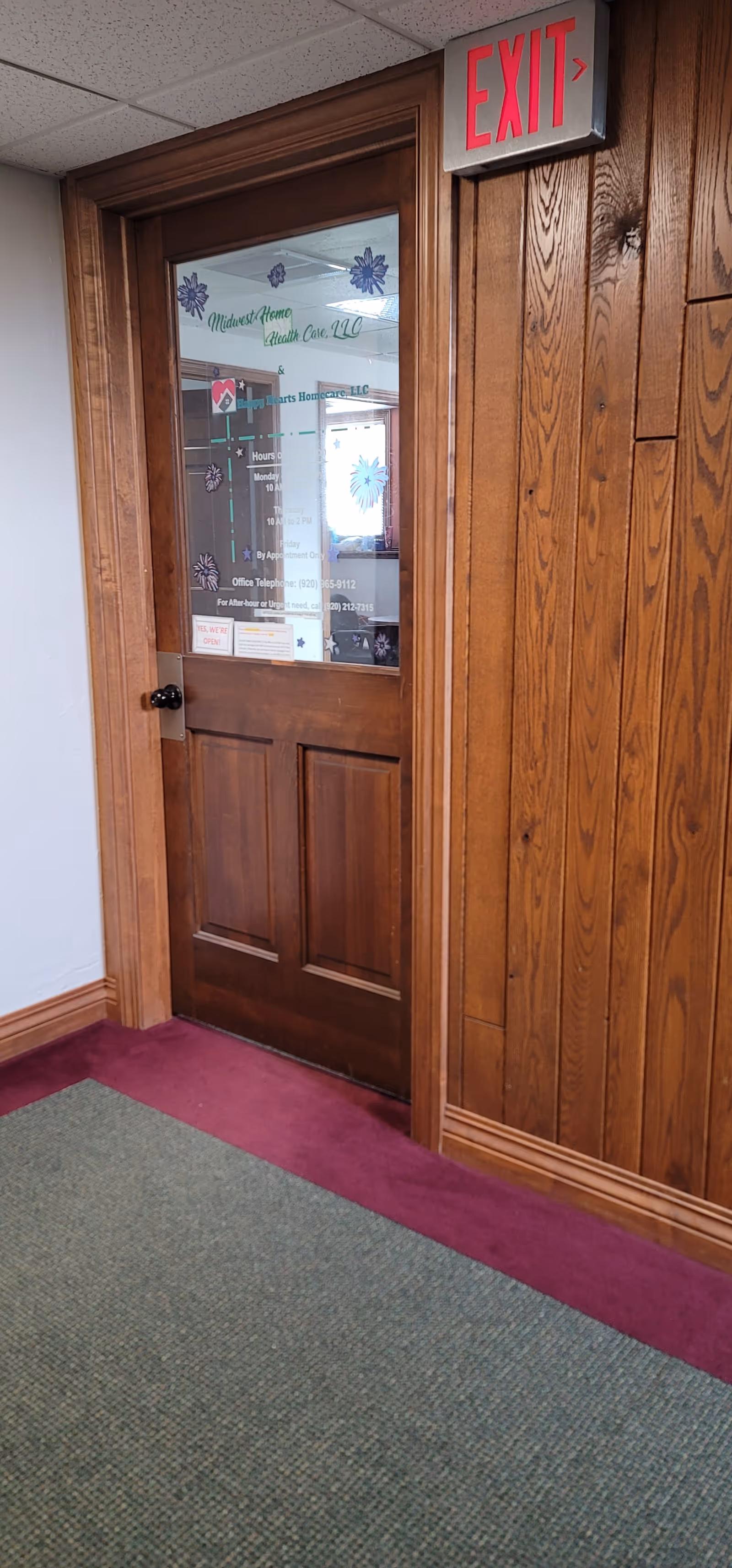 Wood-paneled hallway features a glass door labeled Midwest Home Health Care and an exit sign.