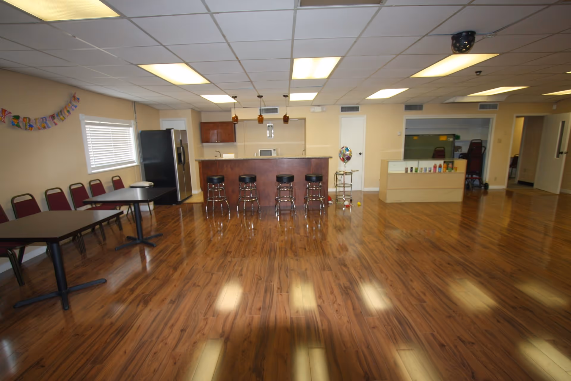 A spacious communal dining area with tables, chairs, a bar counter, and a reception.