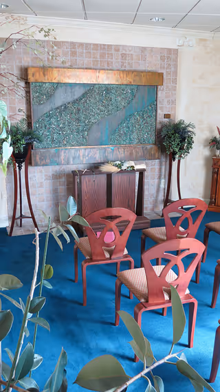 Interior room with blue carpet, red chairs, a wall fountain, and potted plants.