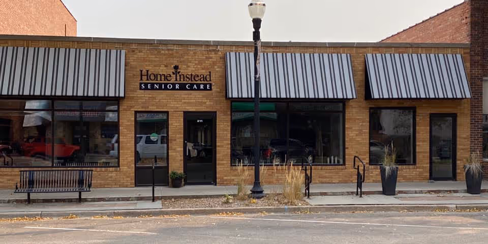 Brick building with Home Instead Senior Care sign and glass storefronts along sidewalk.