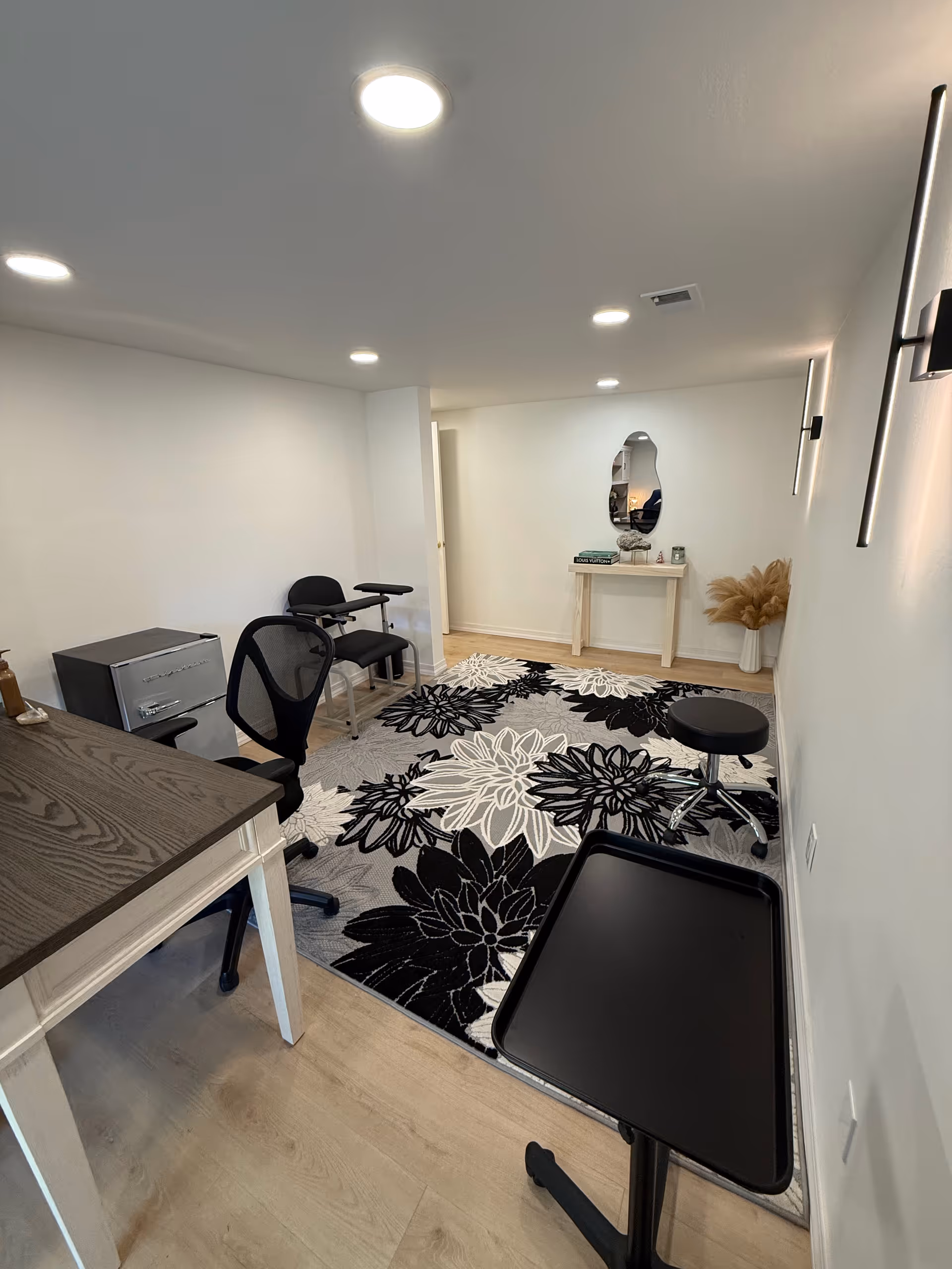 Compact clinic-style office with desk, chair, mirror and floral rug.