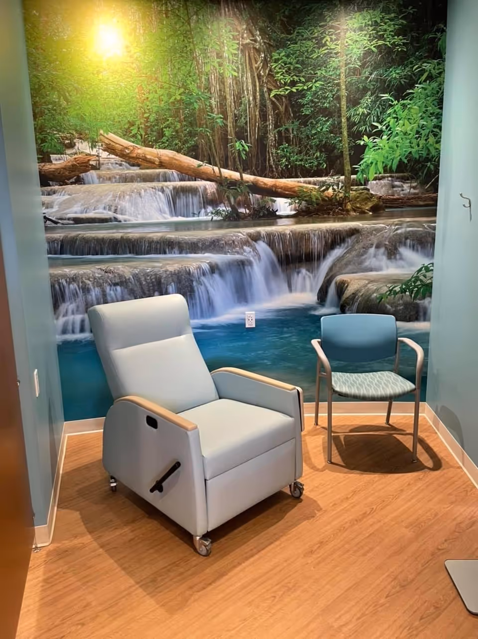 A small therapy room with a waterfall mural and two blue chairs.
