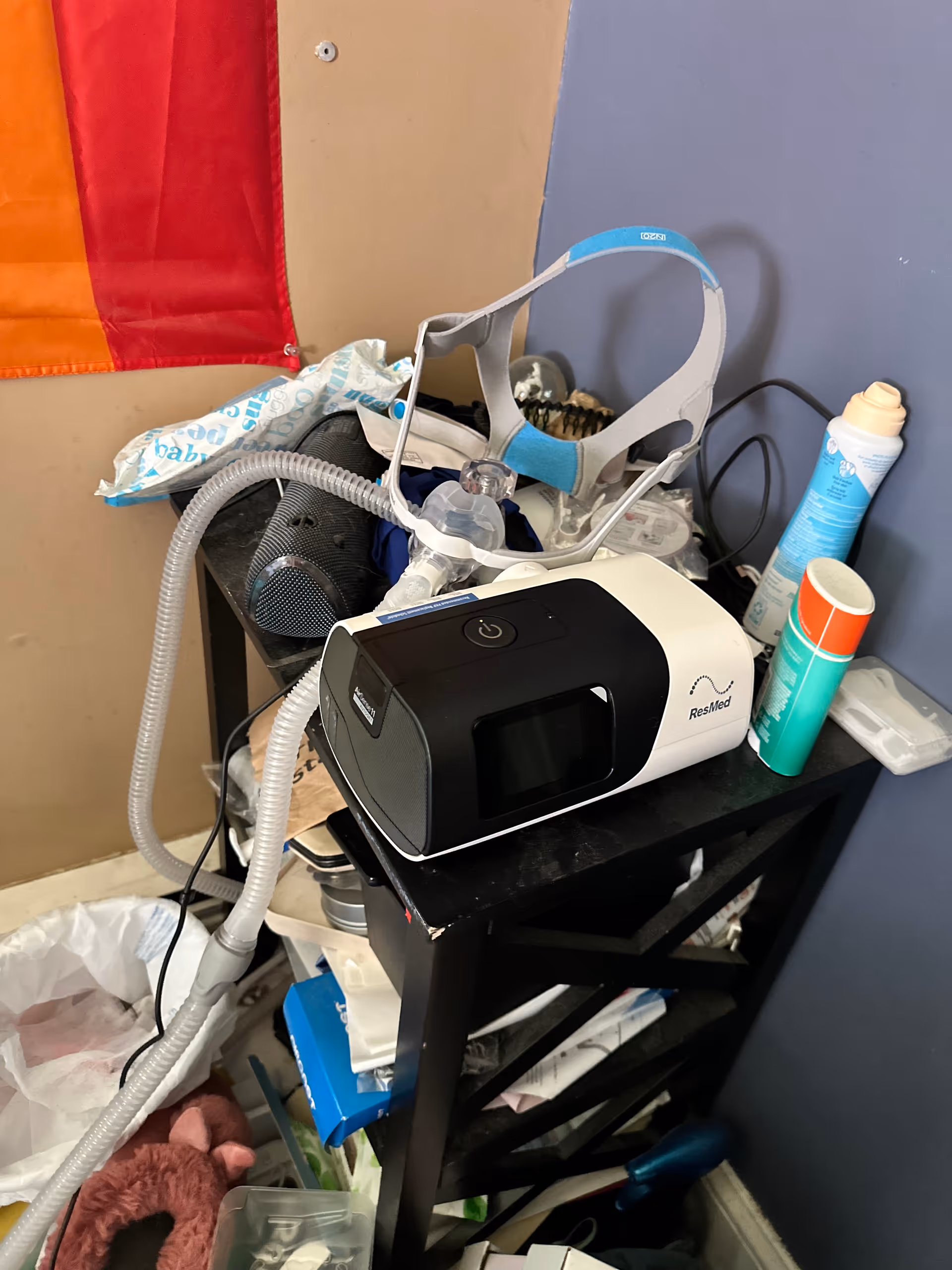 Messy medical equipment on a black cart, including a CPAP machine, mask, hoses, and supplies.