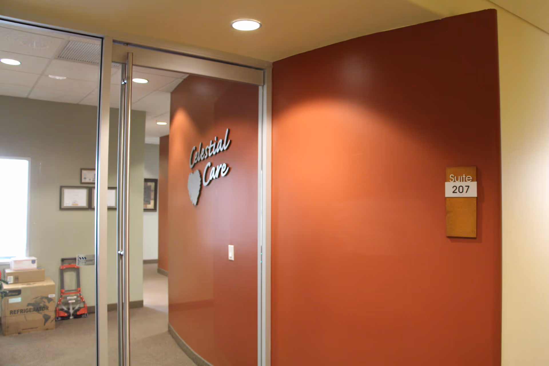 Interior hallway at Celestial Care with glass doors, a red wall, and a Suite 207 sign.