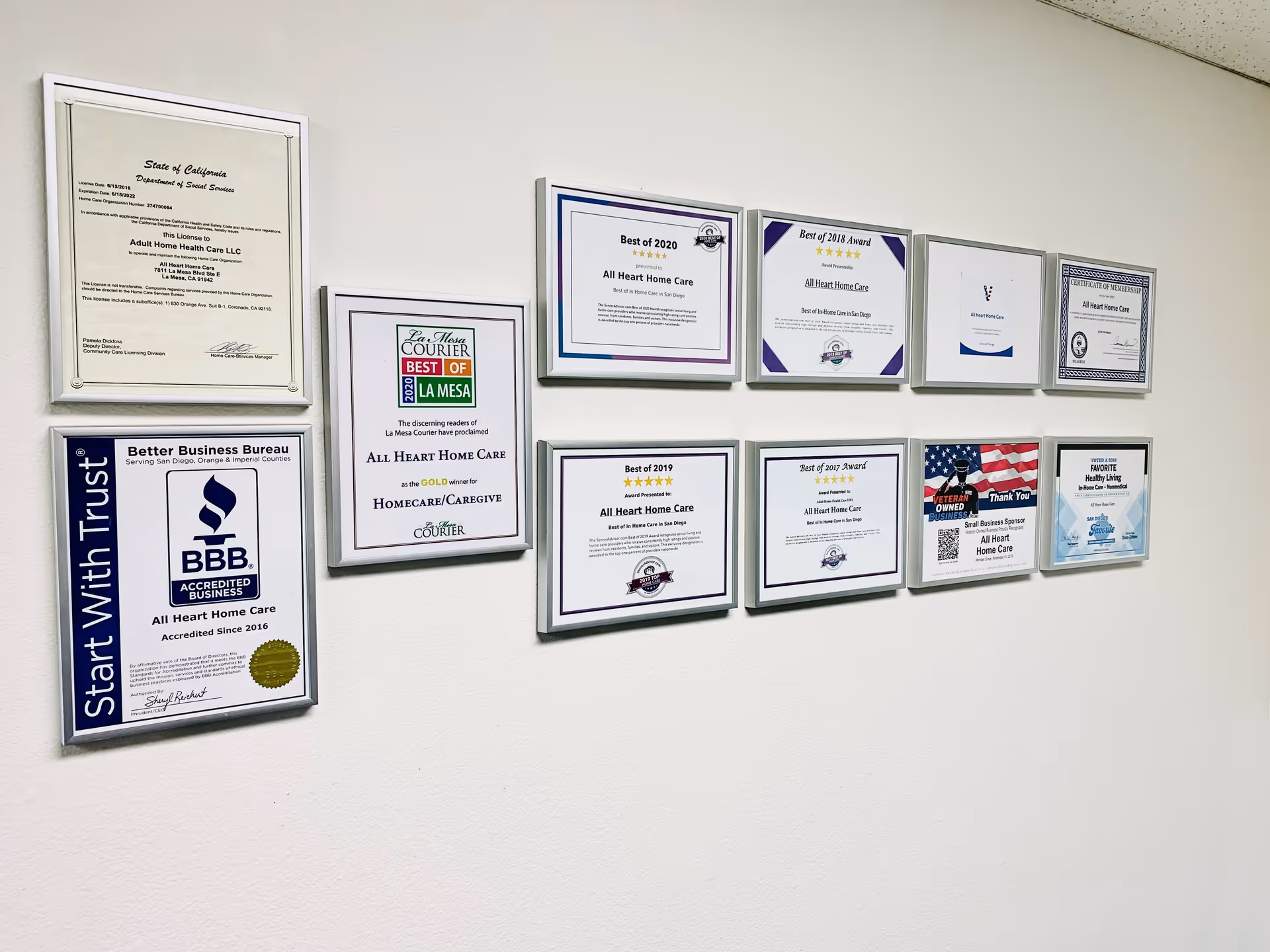 Wall displaying multiple framed awards and certificates for All Heart Home Care in a hallway.