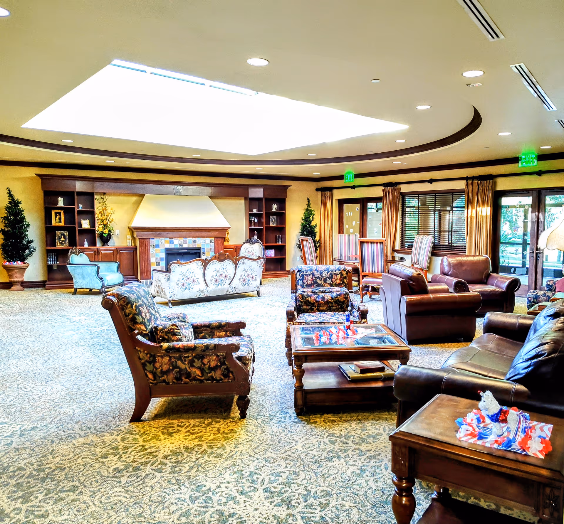 Spacious senior living facility lounge with sofas, chairs, tables, built-in shelves, and a fireplace.