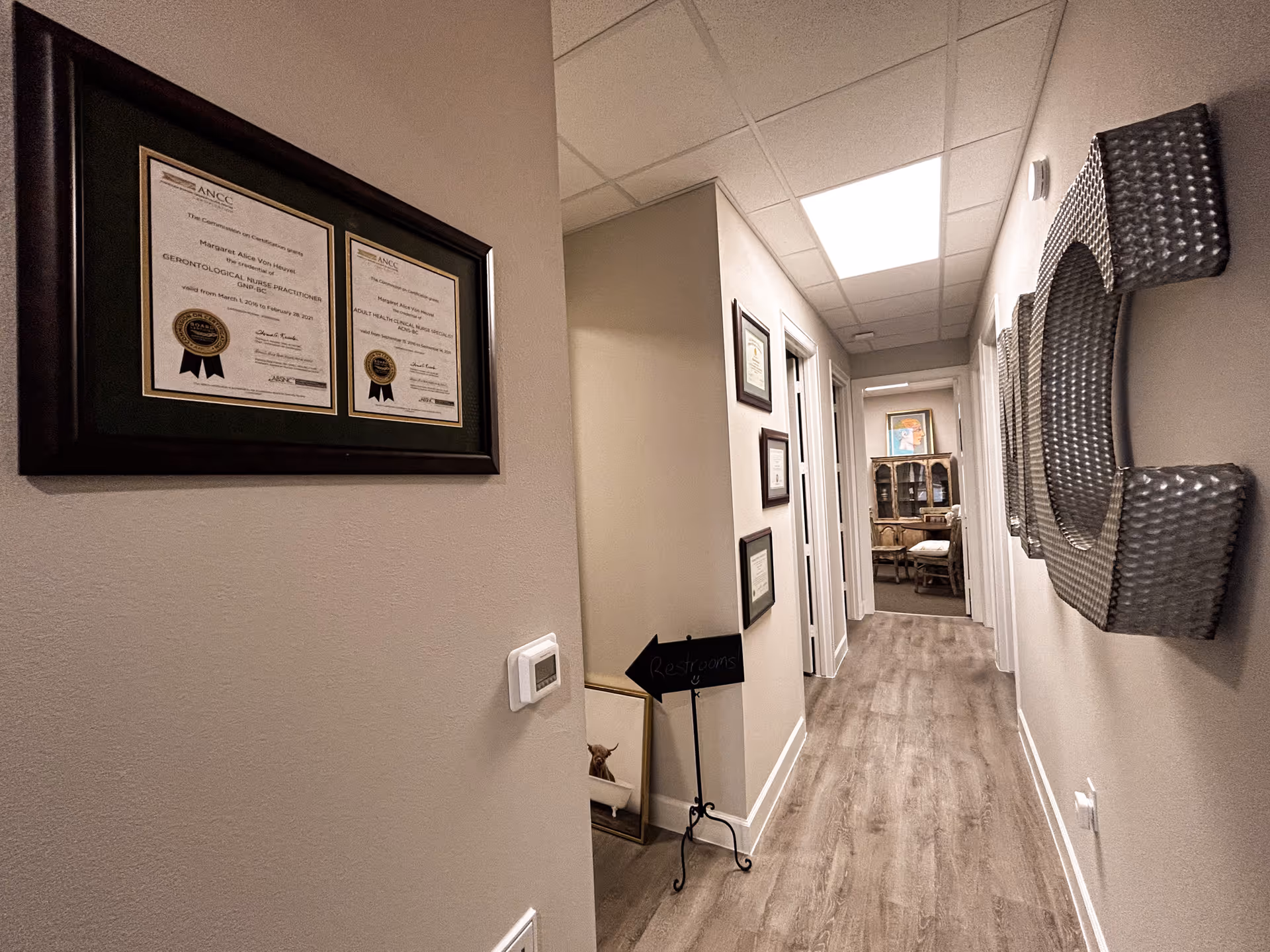 Interior hallway with framed certificates, a restroom sign, and a lounge visible at the end.
