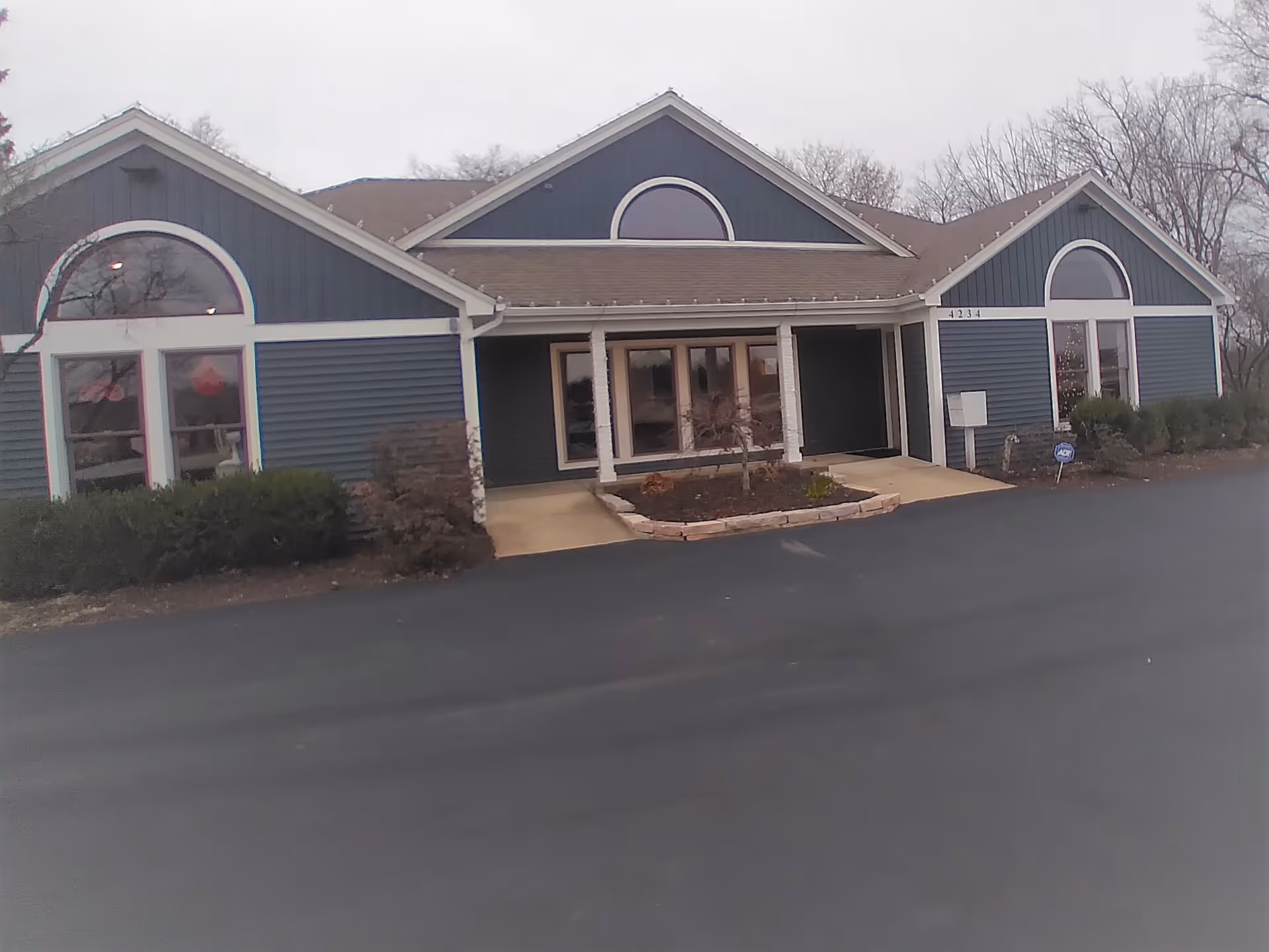 Blue senior living facility with arched windows and glass entrance, parking lot in front.