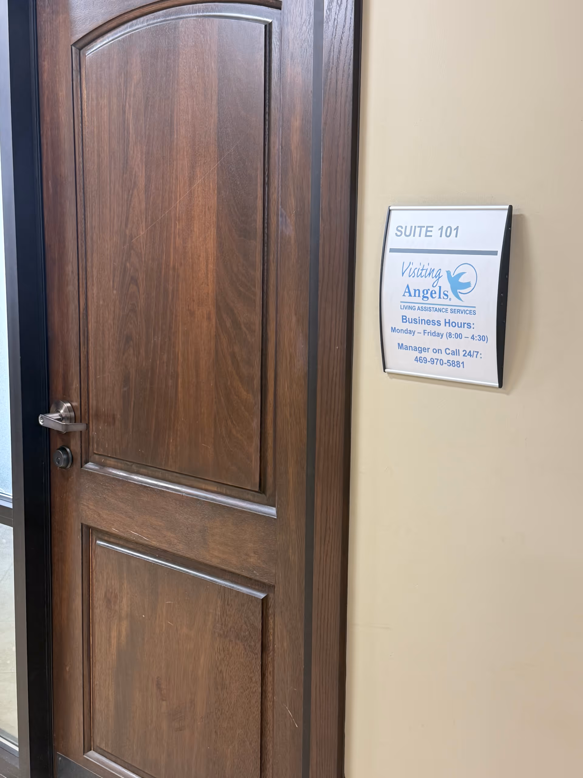 Wooden door beside a wall-mounted Visiting Angels Suite 101 sign in a hallway.