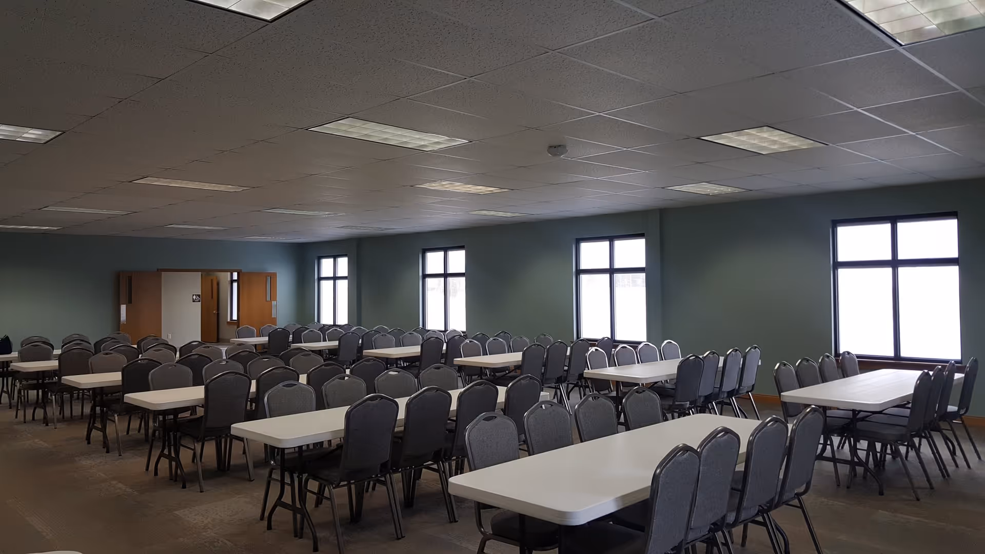 Large hall with many gray chairs around white tables in a bright dining area.