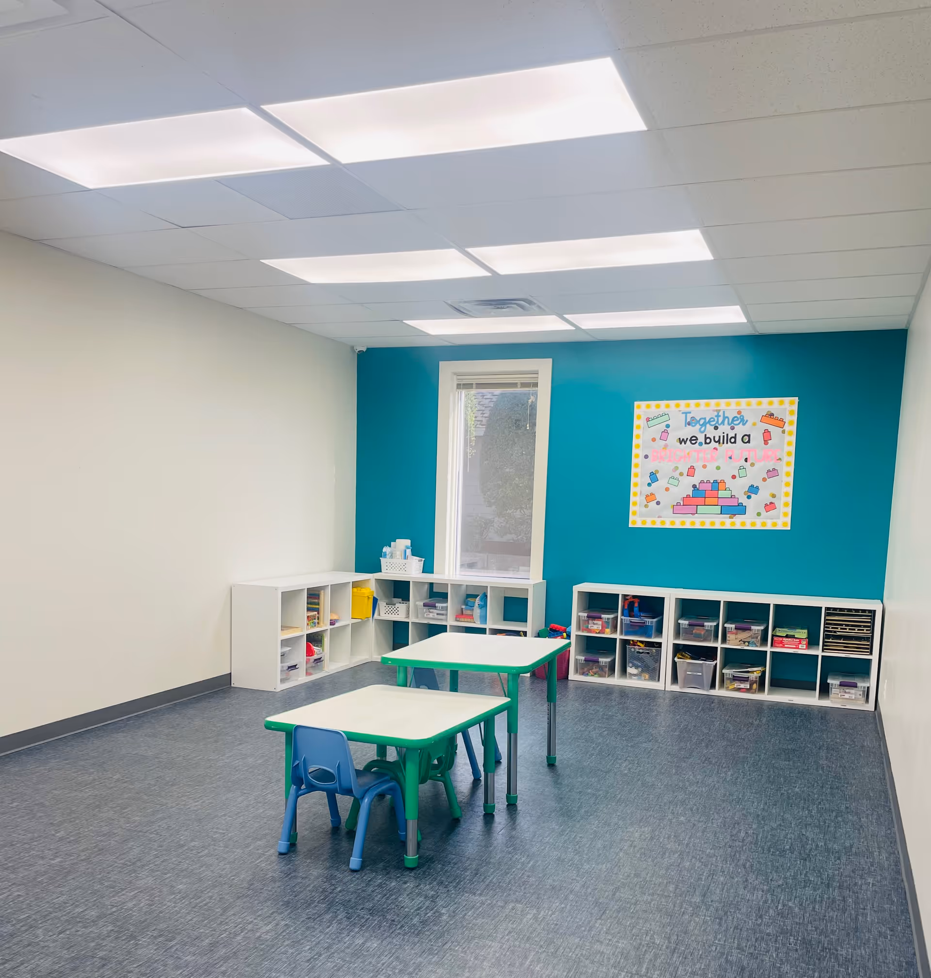 Colorful classroom-like play area with cubbies, tables, and chairs in a bright room.