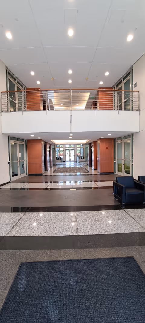 Bright modern lobby with upper balcony, wide hallway, and seating along the right.