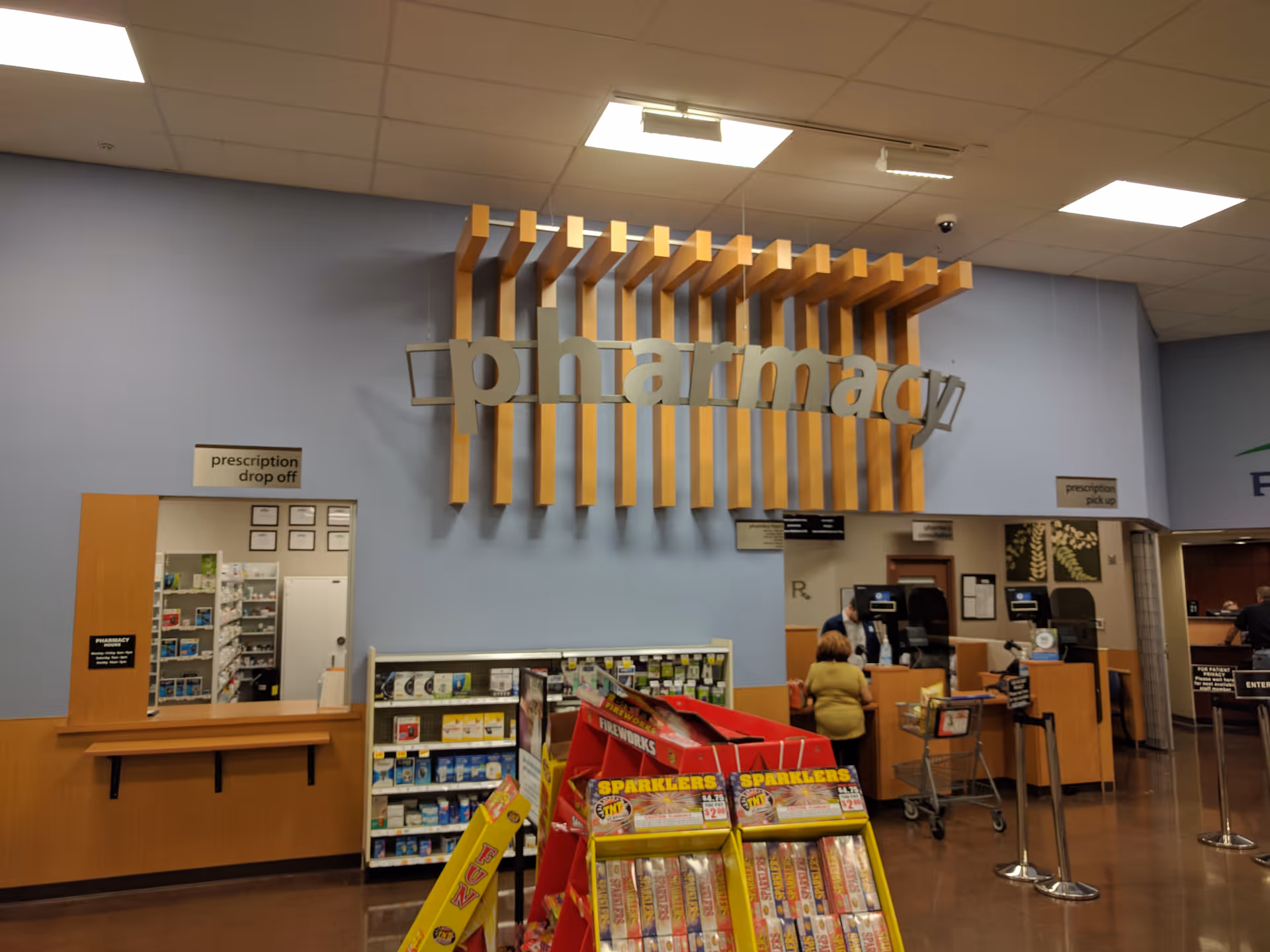 Interior of a Kroger Pharmacy with a large sign, counters, shelves, and customers.