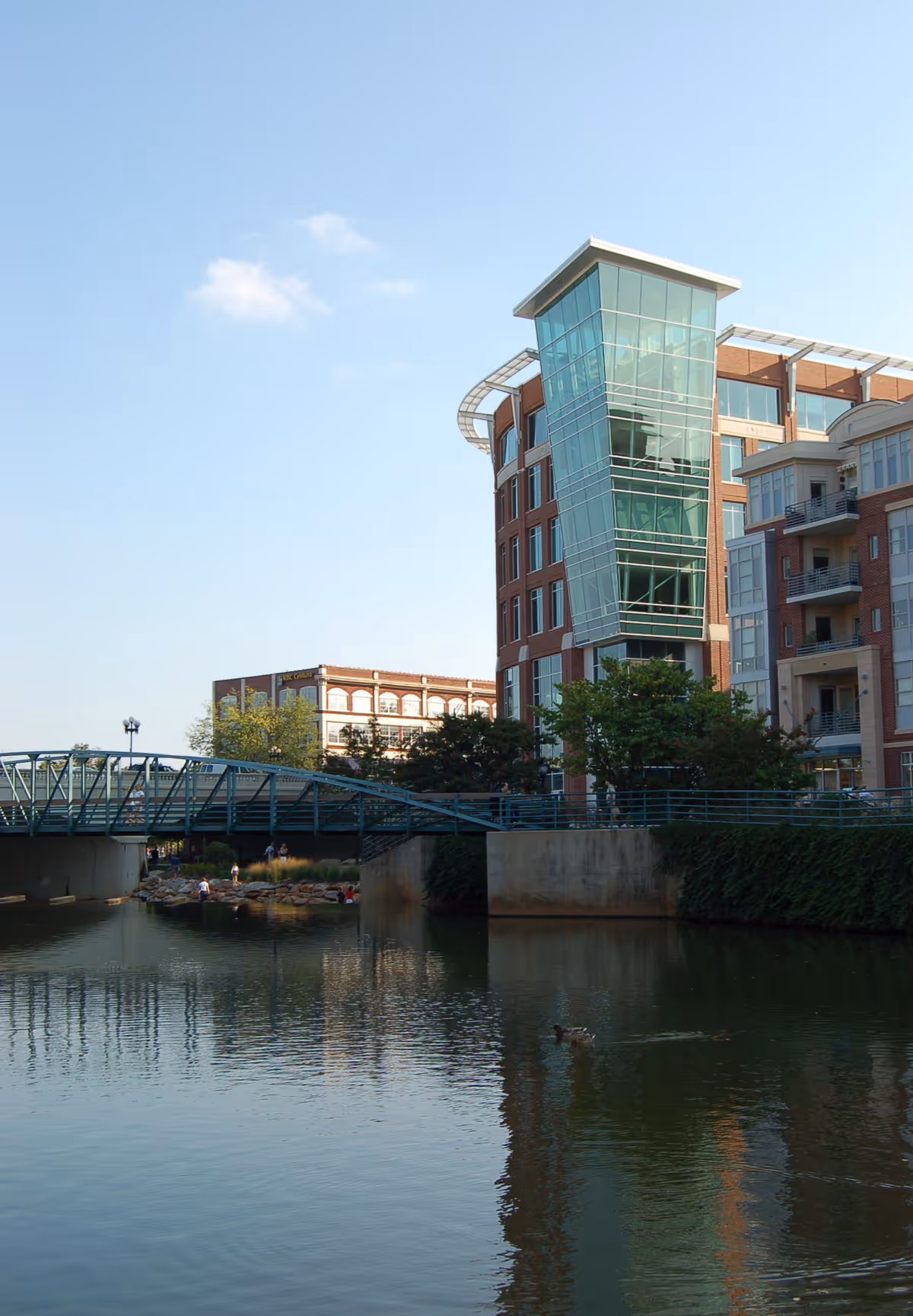 This is a modern riverside senior living building with a glass tower and a pedestrian bridge.