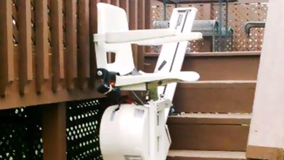 Outdoor wooden deck with a white stair lift chair attached to railing.