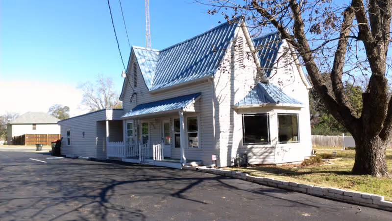 White building with blue metal roof and a large tree in front