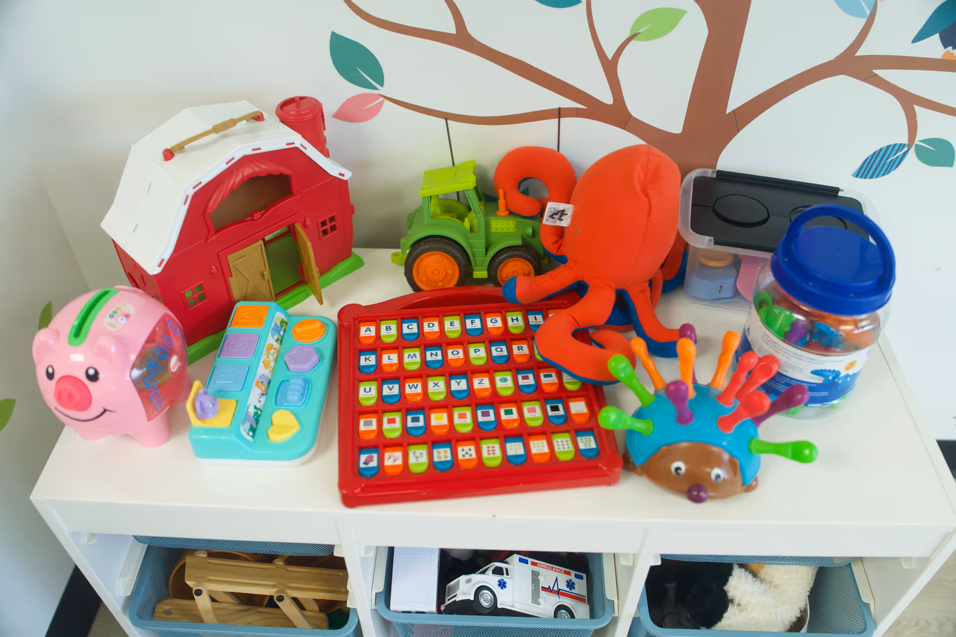 Colorful children's toys displayed on a white shelf against a tree mural.