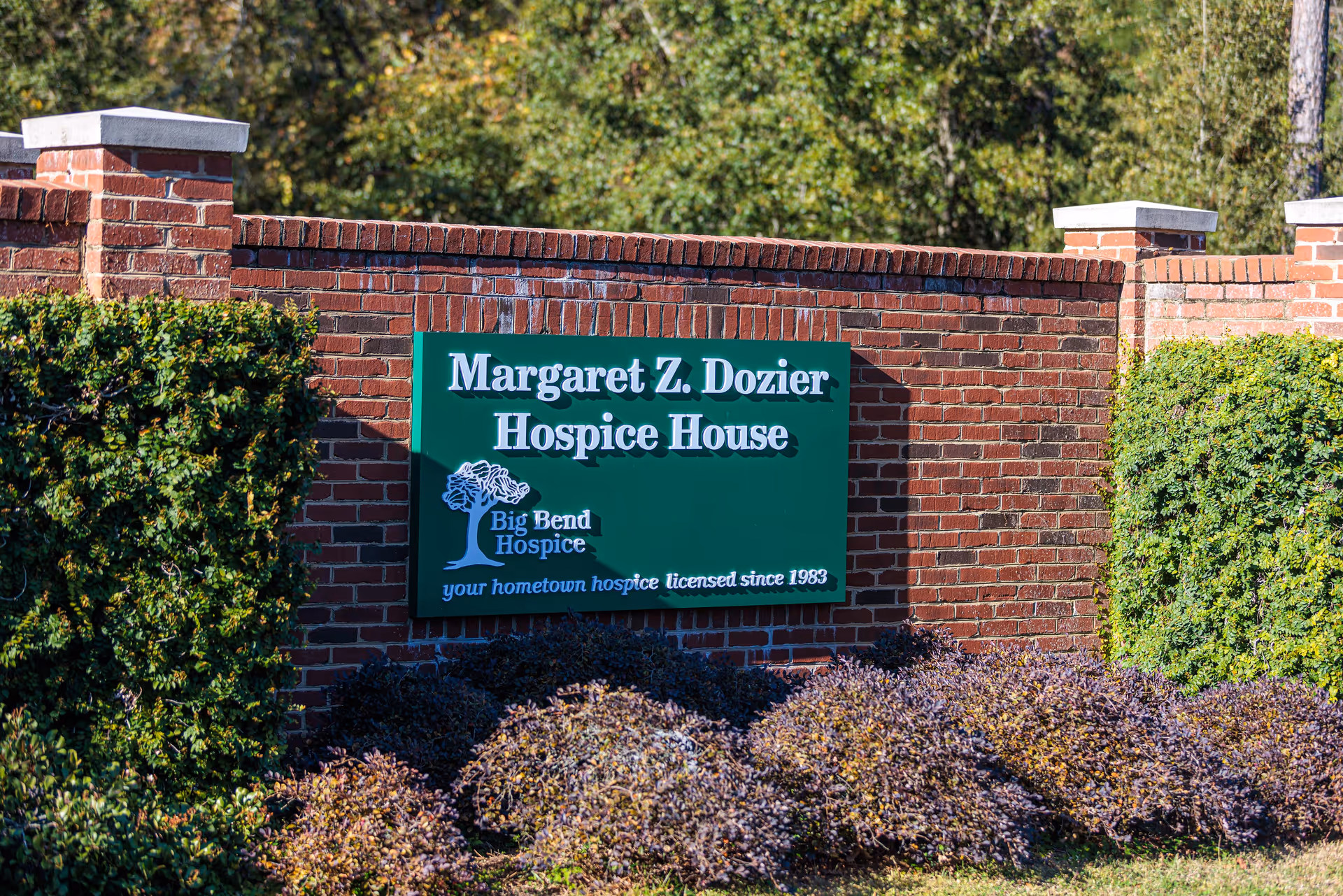 Green sign reading Margaret Z. Dozier Hospice House mounted on brick wall.
