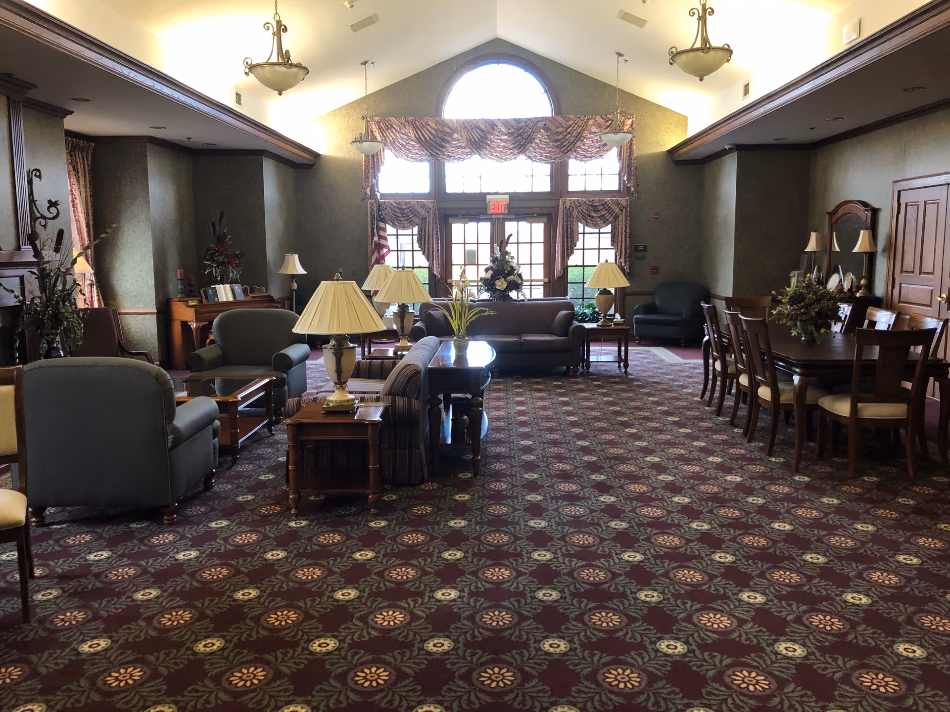 Senior living facility lounge with couches, tables, lamps, and a patterned carpet.