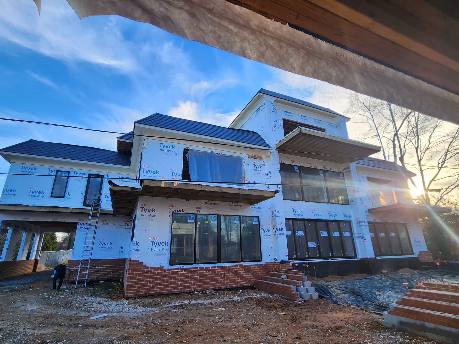 Under-construction two-story building with Tyvek wrap and exposed brick foundation.