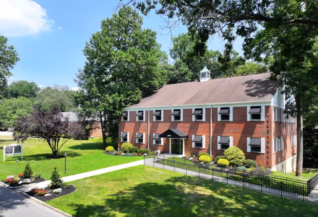 Brick senior living facility exterior with awnings, landscaping, and trees.