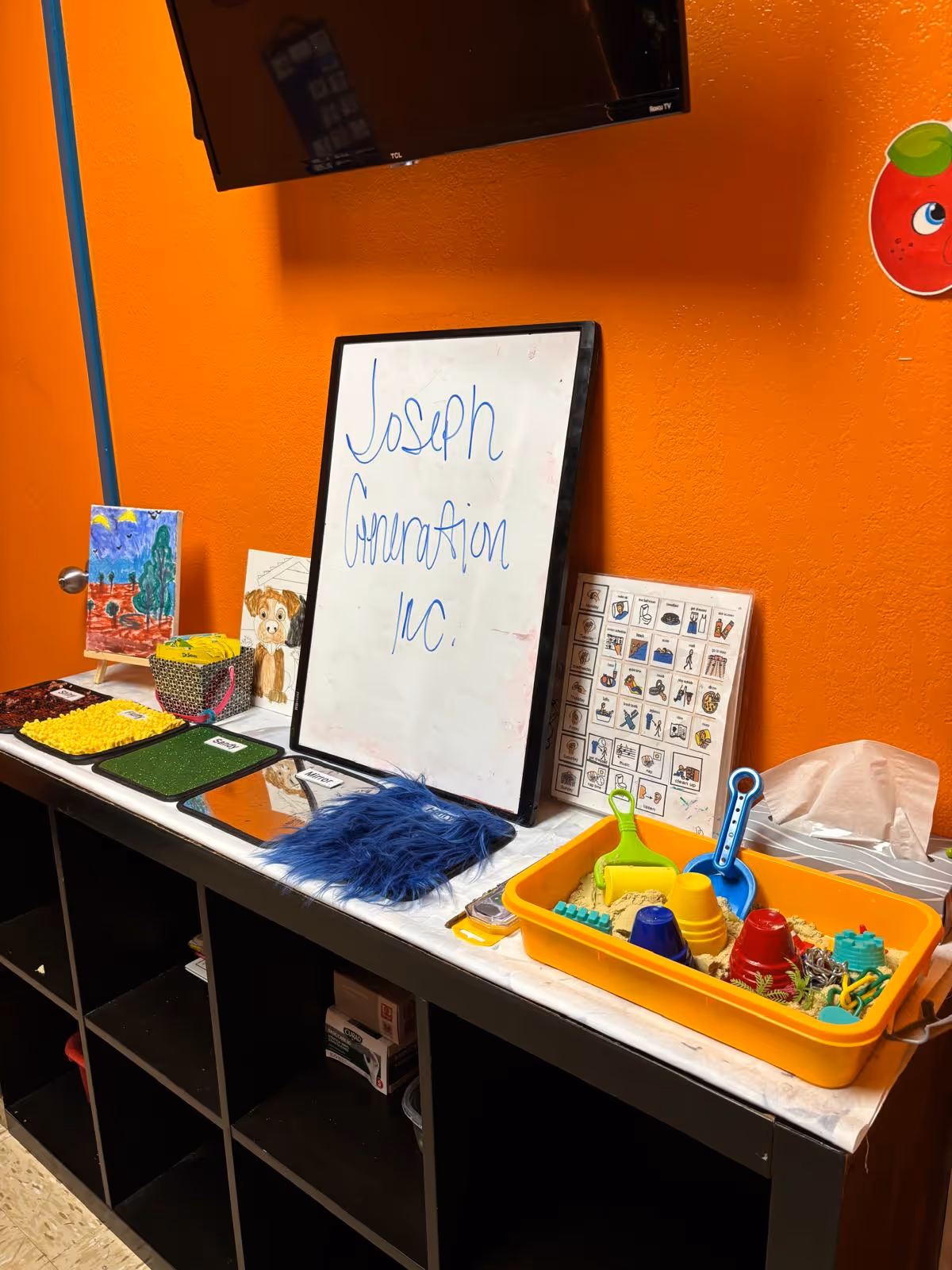 Bright orange interior with a whiteboard reading Joseph Generation Inc. and a toy-filled activity area.