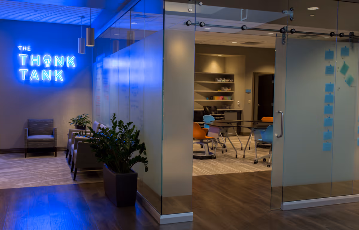A glass-walled lounge labeled The Think Tank features a blue neon sign and colorful chairs.