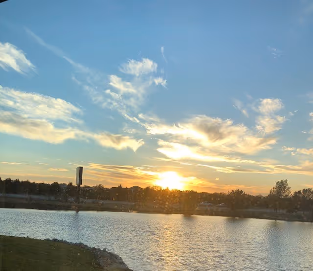 Sunset over a calm lake with a tree-lined shore.